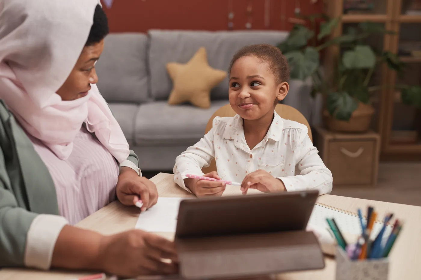 A young girl smiles at her mother across the table while her grandmother holds a tablet